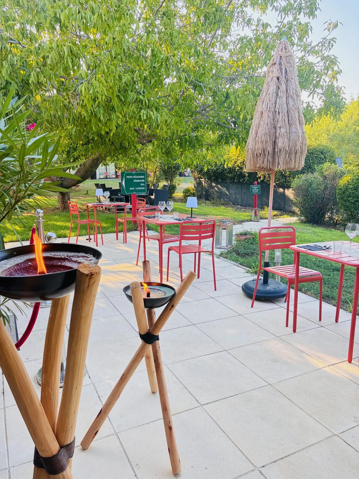 Torches en bambou sur la terrasse, tables rouges et jardin