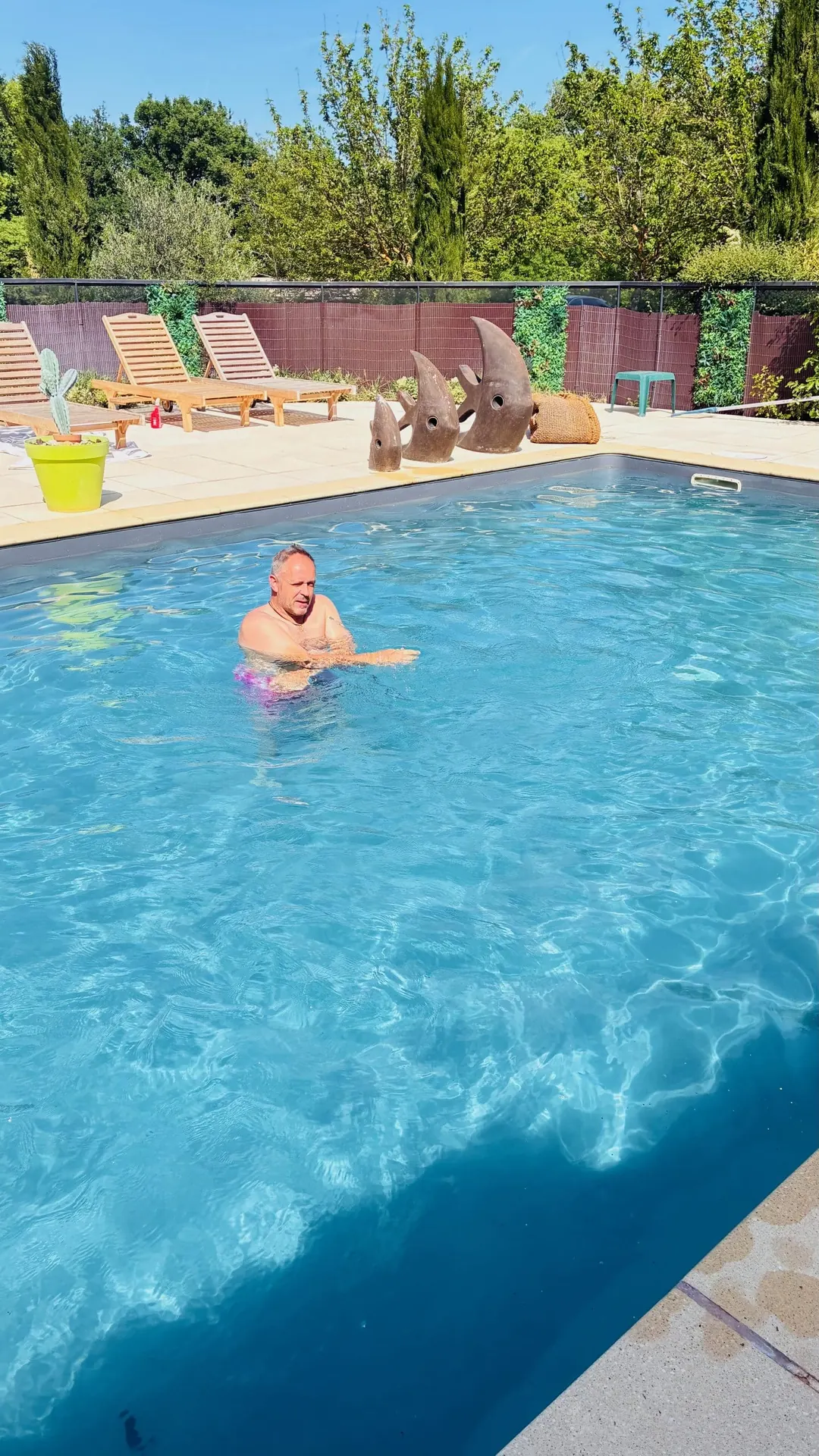 Baigneur dans la piscine au soleil, transats en fond